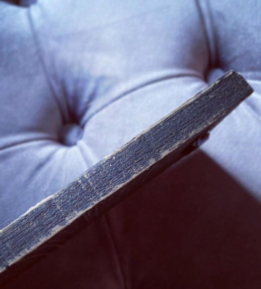 A close-up shot of a dark, weathered wooden board or plank resting diagonally across a tufted gray fabric surface.