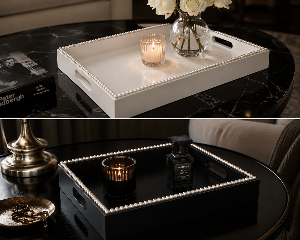A split-screen lifestyle image showing a decorative rectangular tray in two colorways: a white tray with a pearl-like beaded border in the top half, and a black tray with the same beaded border in the bottom half. Both trays are styled on a black marble table with a candle, flowers, and a perfume bottle.