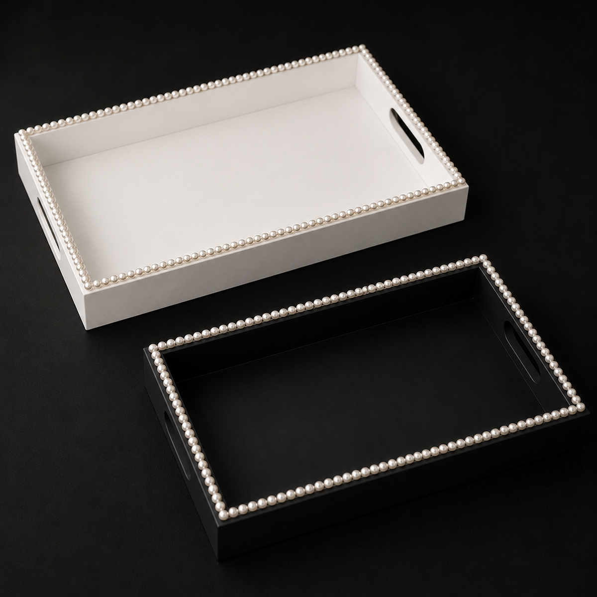 Two rectangular decorative trays with pearl-beaded edges, shown on a black background. One tray is white with a black handle cutout, and the other is black with a matching handle cutout.