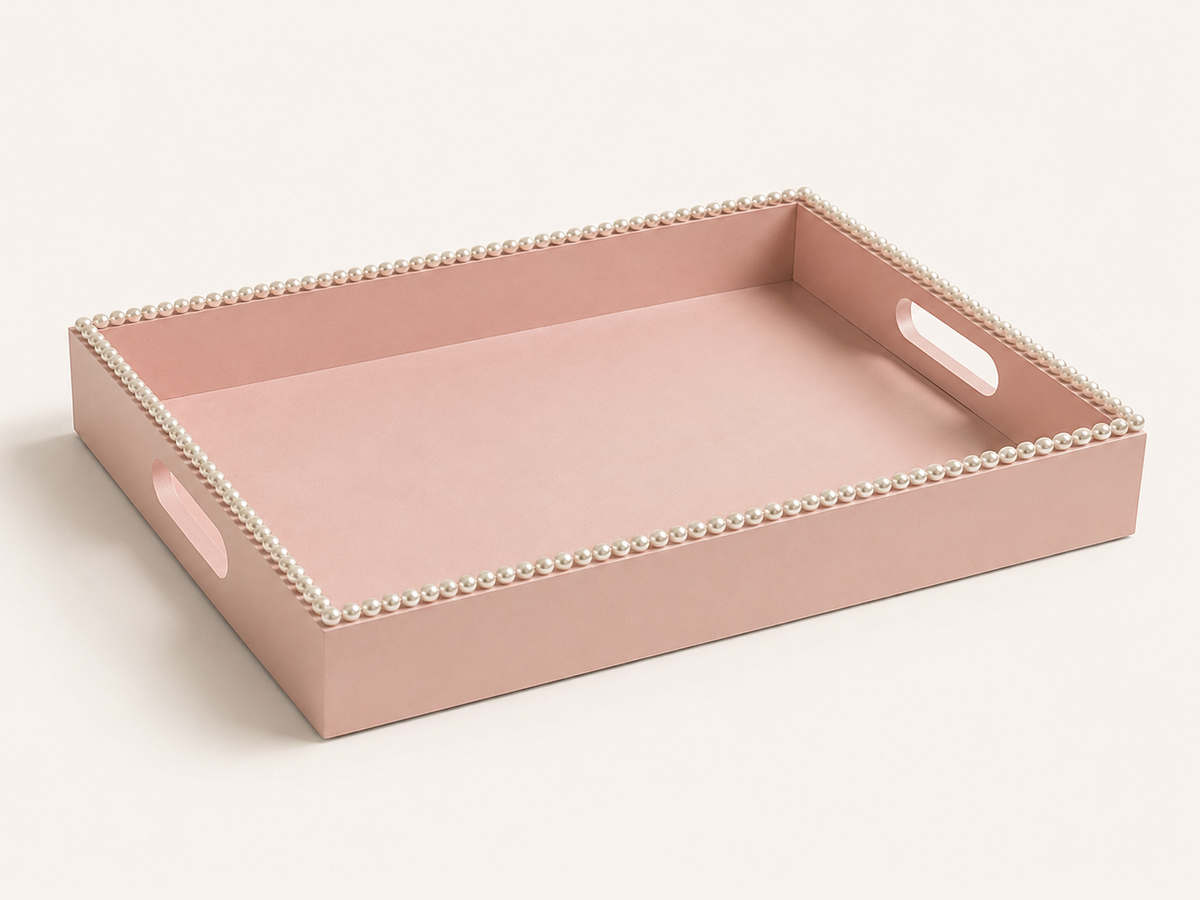 A rectangular blush pink tray with cutout handles and a decorative border of small white pearls, photographed on a clean off-white background.