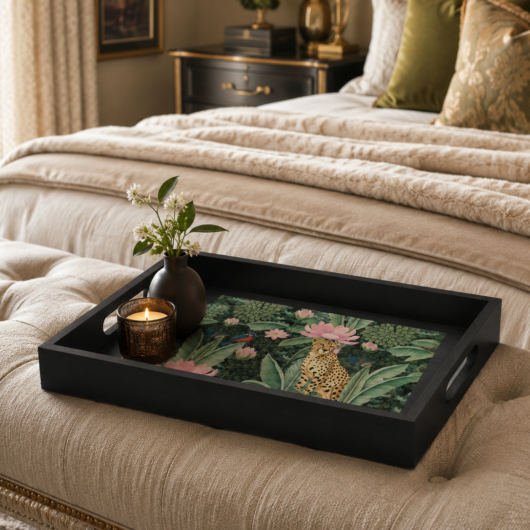 A rectangular black serving tray with a tropical jungle print featuring a leopard, pink flamingos, and green foliage, styled on a beige tufted bench in a bedroom setting.