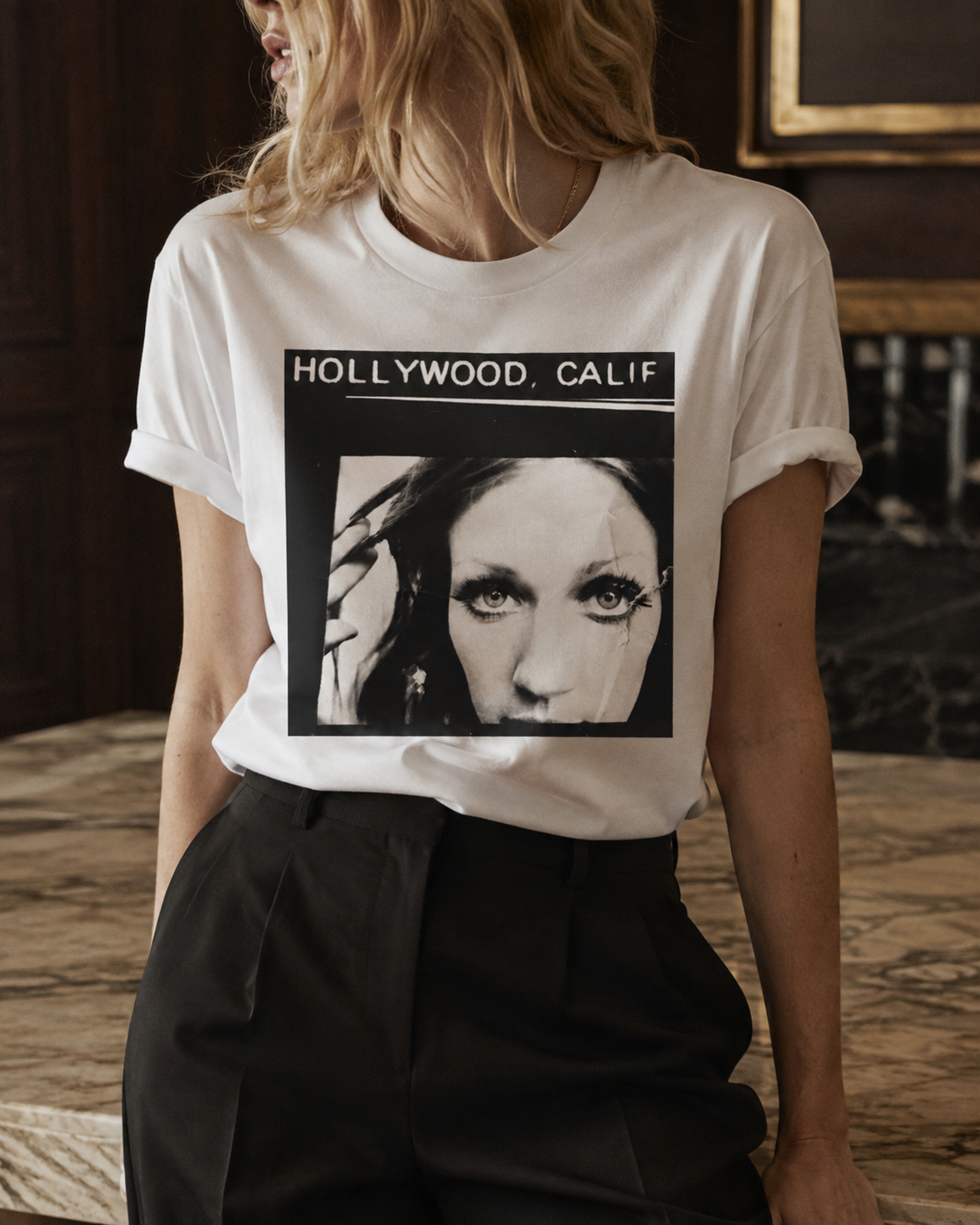 A woman wearing a white graphic t-shirt with a black and white 'Hollywood. Calif.' photographic print.
