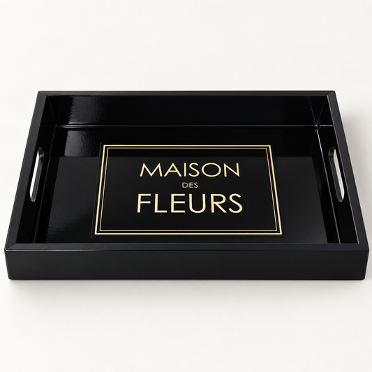 A black rectangular serving tray with side handles and a glossy finish, featuring a gold-bordered label that reads 'MAISON DES FLEURS' in gold lettering in the centre.
