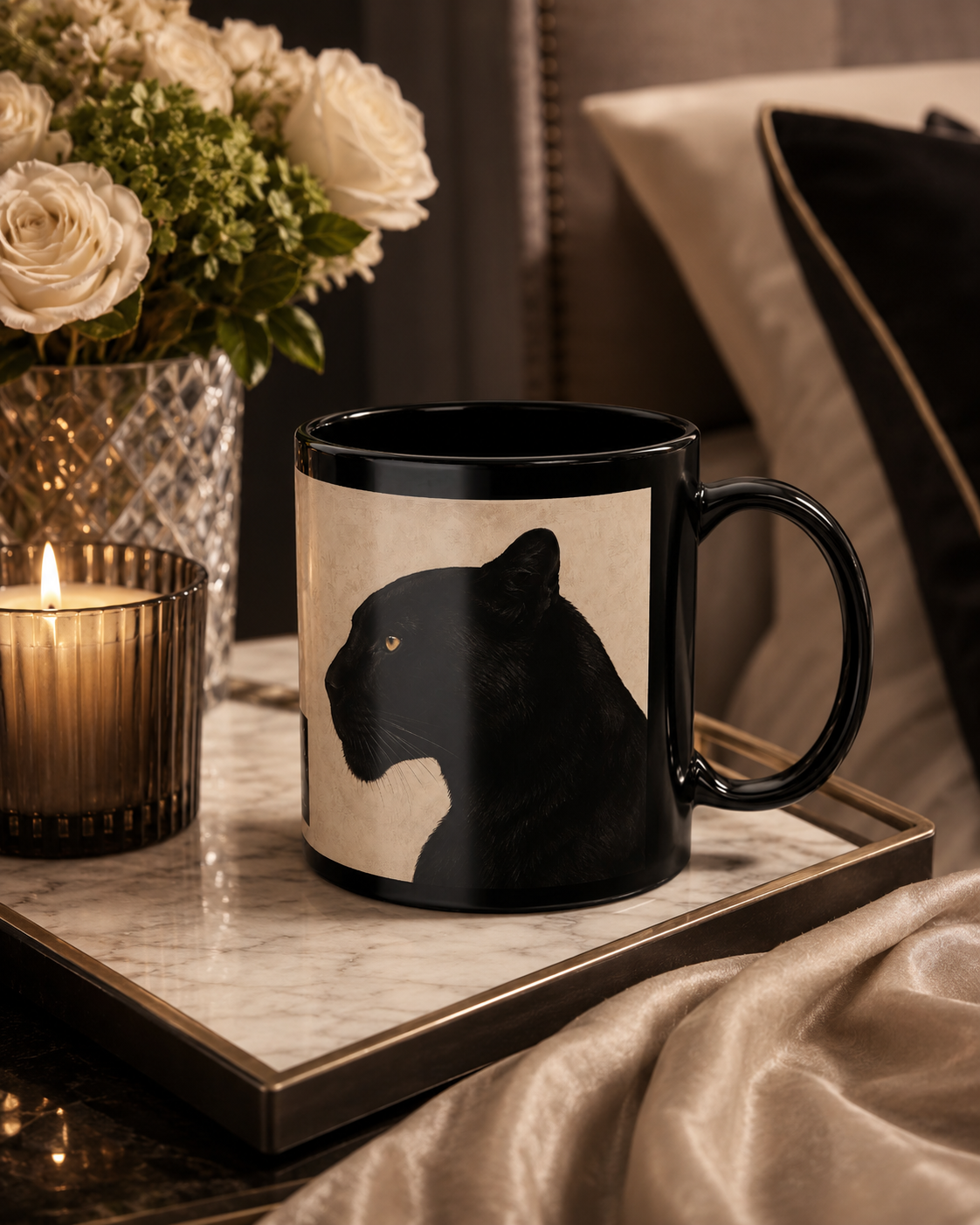 A black ceramic mug with a cream-colored panel featuring a black panther illustration, styled on a marble tray next to a lit candle and flowers.