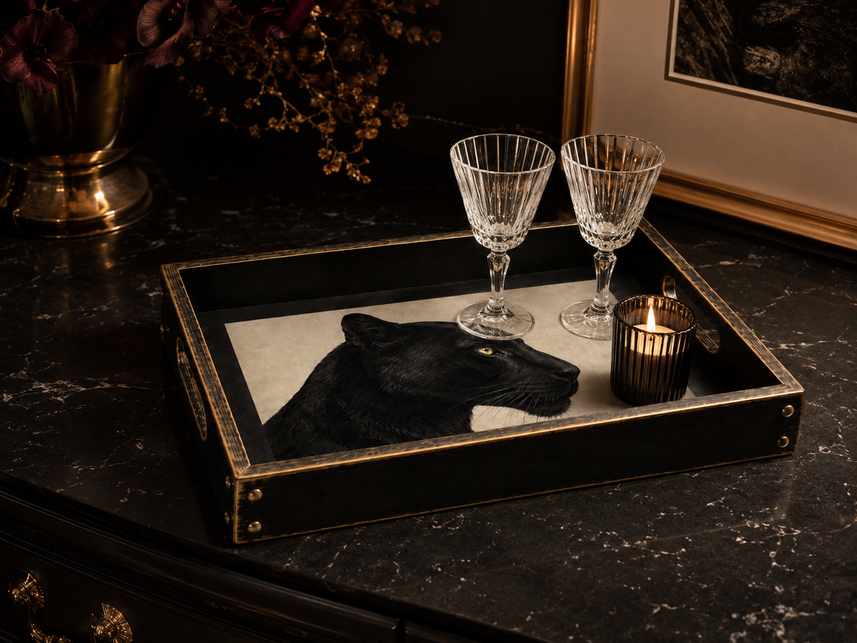 A black rectangular decorative tray with gold trim and corner protectors, styled on a dark marble surface. The tray features a black panther head design, two clear cut-crystal wine glasses, and a small lit candle.
