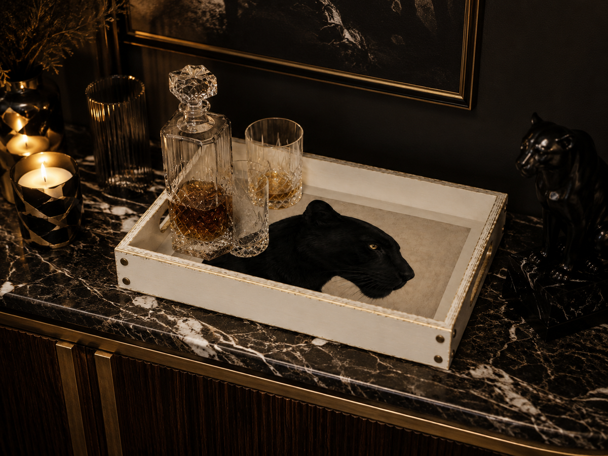 A rectangular white tray with a black panther head centrepiece, styled on a dark marble console table with a decanter, two glasses, candles, and a black panther figurine in a moody interior setting.