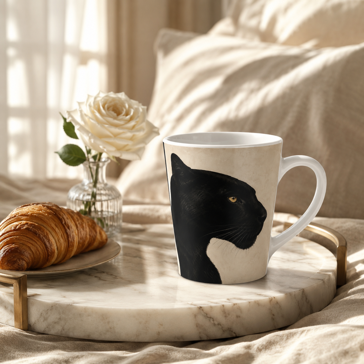 A black panther mug on a marble tray with croissant and white rose in a vase, with beige cushions and window drapes in the background with sunshine flowing through.